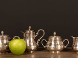 five silver teapots and an apple on a table