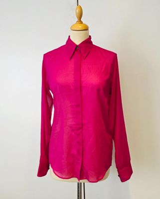 La chemise rose est posée sur un présentoir à mannequin, devant un fond blanc.