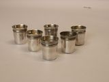 six verres à shot en argent alignés sur une surface blanche