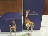 deux figurines de girafes posées sur une table, à côté d'une boîte bleue