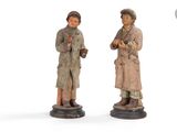two figurines of two people standing next to each other on a white surface