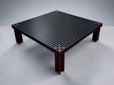 une table noire parsemée de points rouges, posée sur une surface blanche