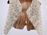 cream and pink floral shrugr on a hanger against a gray background