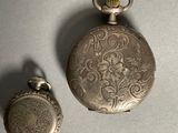 a silver pocket watch and a silver pocket watch on a table