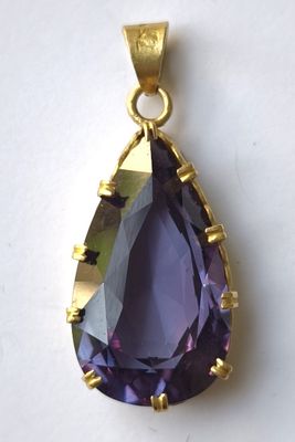 un gros plan d'un pendentif violet en forme de larme posé sur une surface blanche