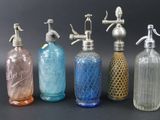 six bouteilles en verre de couleurs différentes sont alignées sur une surface noire