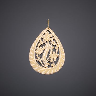 a gold tear shaped pendant with a floral design