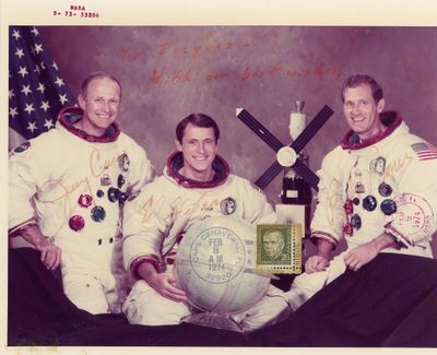 Deux hommes vêtus de combinaisons spatiales blanches posent pour une photo avec un globe terrestre