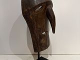 a close up of a wooden mask on a stand on a white surface