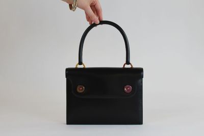 la main d'une femme tenant un sac à main noir sur fond blanc
