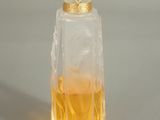 flacon de parfum avec un bouchon en verre et un bord doré sur un fond gris