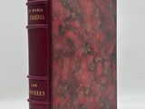 an old book with a red cover sitting on top of a white surface