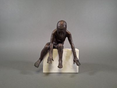 statue of a man sitting on a block with his hands on his knees