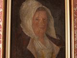 portrait d'une femme coiffée d'un bonnet blanc, dans un cadre doré, accroché à un mur tapissé de papier peint rose