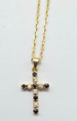 un pendentif en forme de croix en or, orné de pierres noires et blanches, monté sur une chaîne