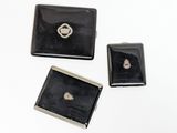 three small black and silver jewelry pieces sitting on top of a white surface