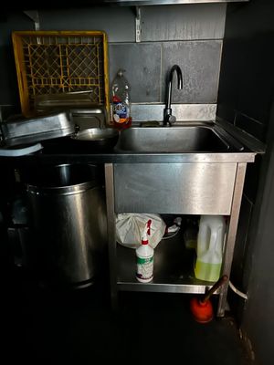 a sink in the corner of a kitchen with a trash can