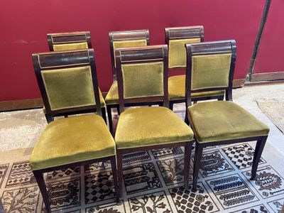 Quatre chaises aux assises recouvertes de velours vert sont disposées devant un mur rouge.
