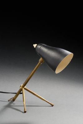 une lampe noire et dorée posée sur un trépied, devant un fond noir