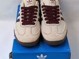 une paire de baskets blanches avec des lacets bordeaux posée sur une boîte bleue