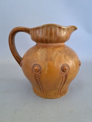 un vase marron muni d'une anse, posé sur une table blanche