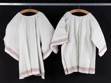 pair of white blouses hanging on a clothes rack in front of a black wall