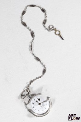une montre de poche en argent avec une chaîne, posée sur une surface blanche