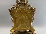 une image représentant une horloge en or posée sur un socle, surmontée d'un oiseau