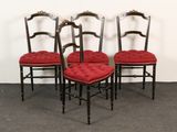 four chairs with red upholstered cushions sit in front of a white wall