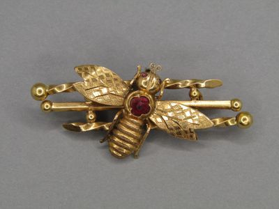 an image of a gold bee brooch with garnetts on it