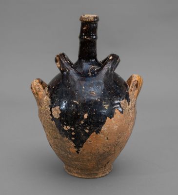 an old black and brown vase with a handle on a gray surface