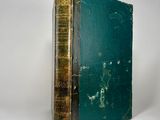 an old book with a green cover sitting on a white surface