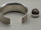two silver bracelets and a silver ring on a white surface