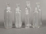 four clear glass bottles with white caps are lined up on a gray surface