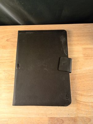 un étui en cuir noir pour iPad posé sur une table en bois à côté d'une chaise noire