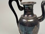a silver tea pot with a handle on a stand