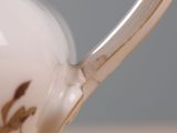 a white tea pot with a gold decoration on it