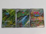 Trois cartes Pokémon sont posées sur une table blanche