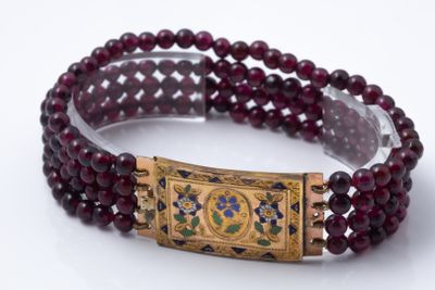 a close up of a bracelet with red beads and a gold clasp