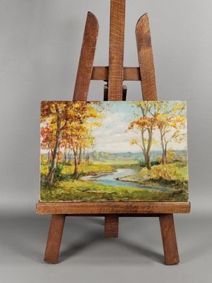 un chevalet sur lequel est posé un tableau représentant une rivière et des arbres