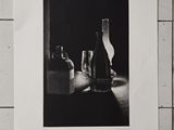une photo en noir et blanc représentant une bouteille de vin et un verre posés sur une table