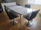 une table blanche avec des chaises noires et une télévision en arrière-plan