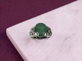 an emerald and diamond ring sitting on a marble slab