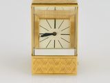 une petite horloge dorée avec un cadran noir sur un fond blanc