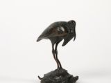 statue en bronze représentant un oiseau posé sur un rocher, sur fond blanc