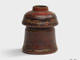 un vase marron surmonté d'un couvercle rouge, posé sur une surface blanche