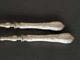 two silver spoons with ornate designs on them sitting on a black surface