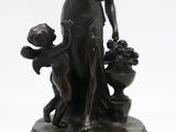 une statue antique en bronze représentant une femme et deux chiens, posée sur un socle en bois