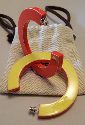 une paire de boucles d'oreilles créoles en acrylique rouge et jaune posées sur un sac