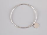 a silver bang bracelet with a disc charm on it